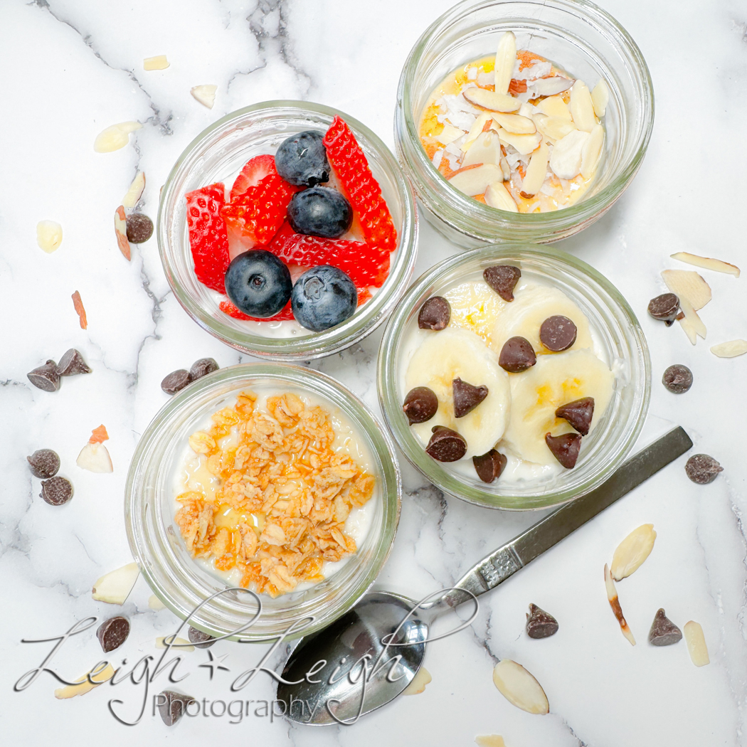 four jars of overnight oats with different toppings, a spoon, and scattered ingredients around them