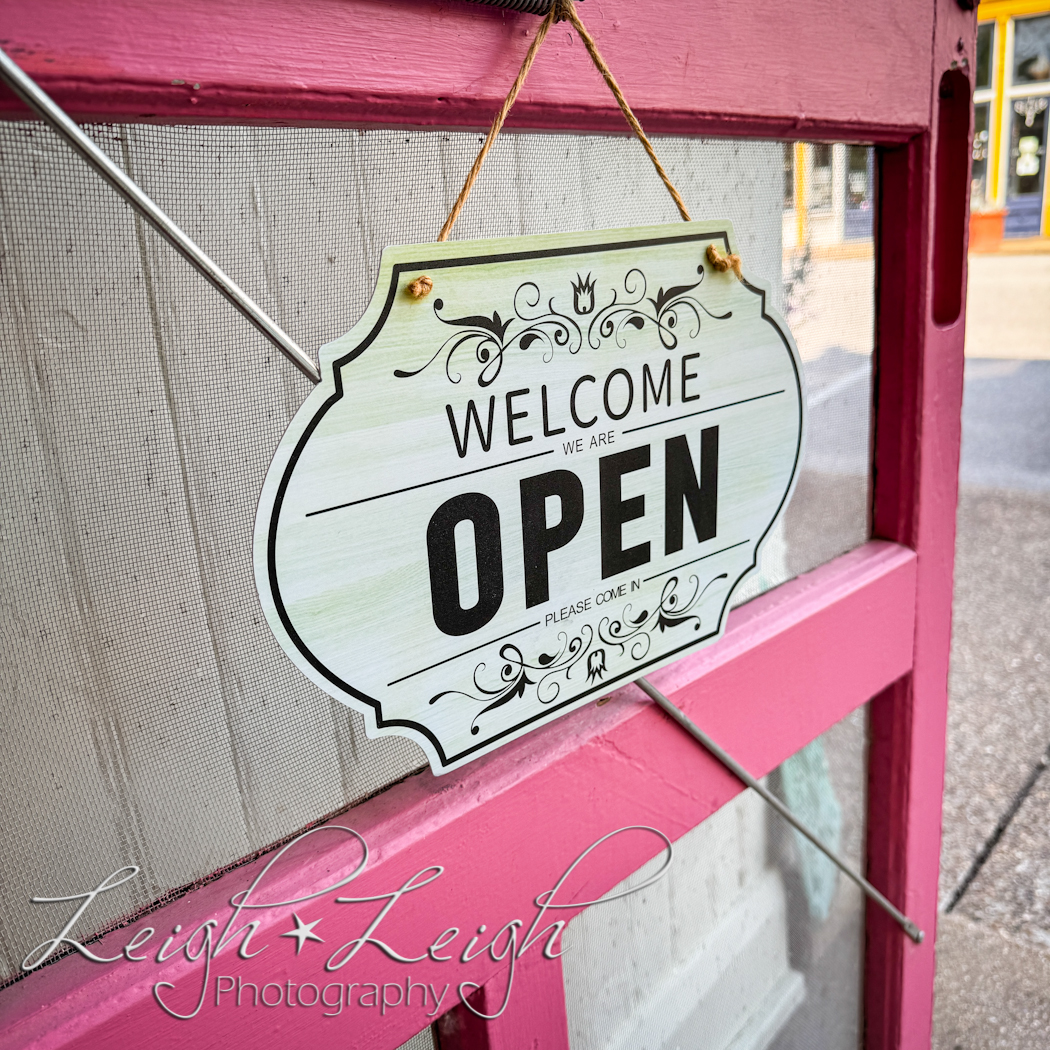 a "welcome we're open" sign on a pink door