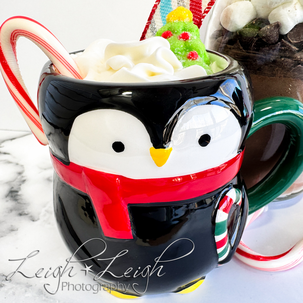 penguin mug of hot chocolate with whipped cream, a candy cane, and a tree marshmallow