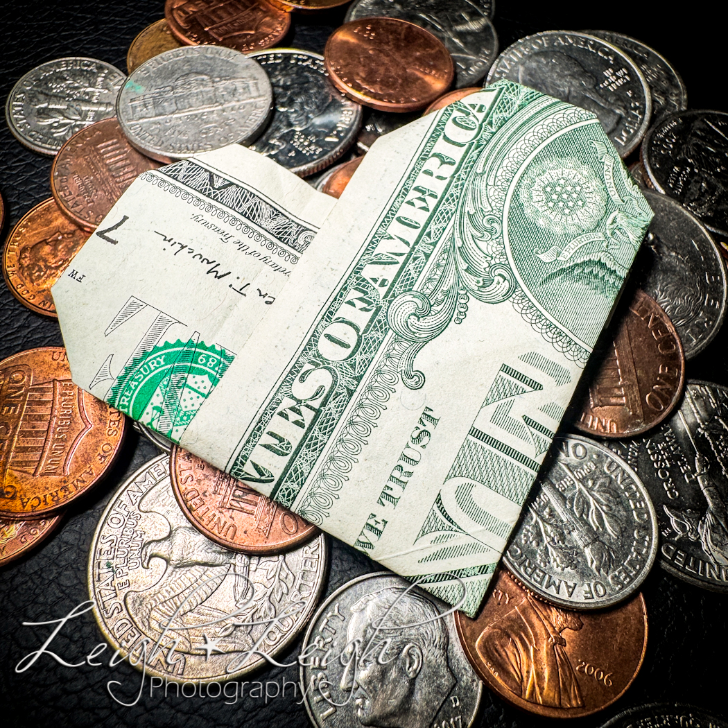 a dollar bill folded into a heart sitting on top of change