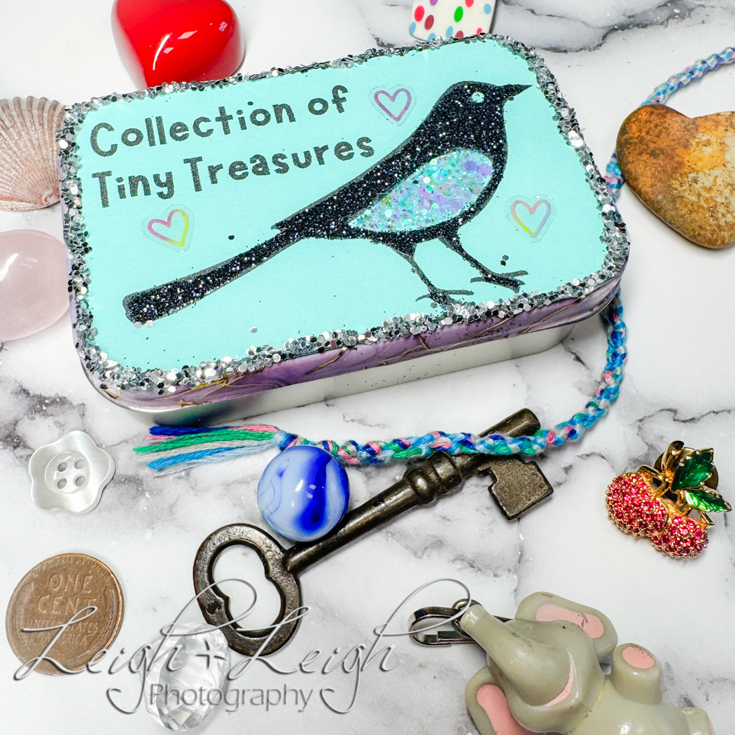 Decorated Altoids tin with a little bird on it that says "collection of tiny treasures", surrounded by random little things like a key, penny, rock, shell, pin, etc.