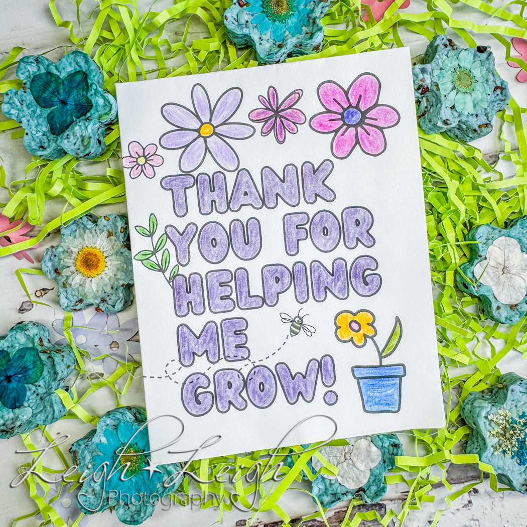 a hand made card that reads: thank you for helping me grow, surrounded by fake grass and seed bombs