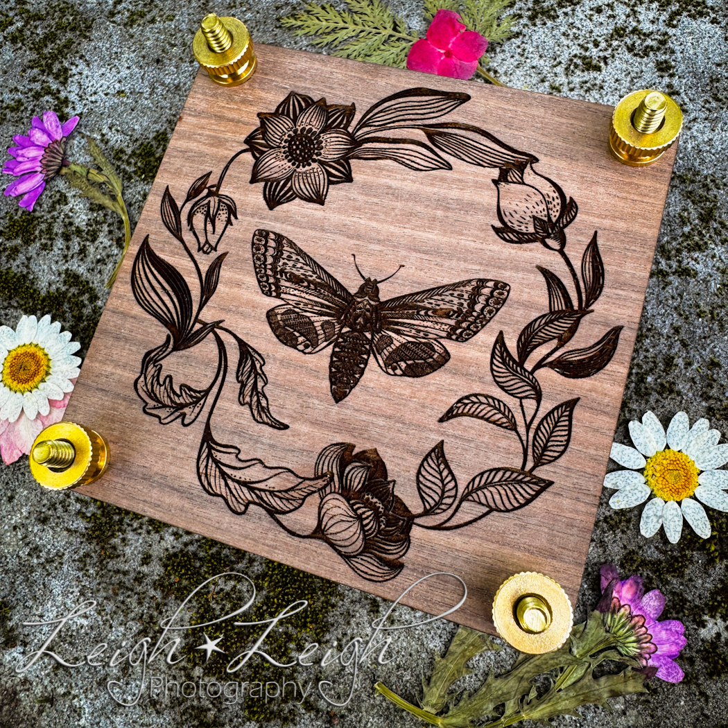 beautifully engraved flower press sitting on a rock surrounded by pressed flowers